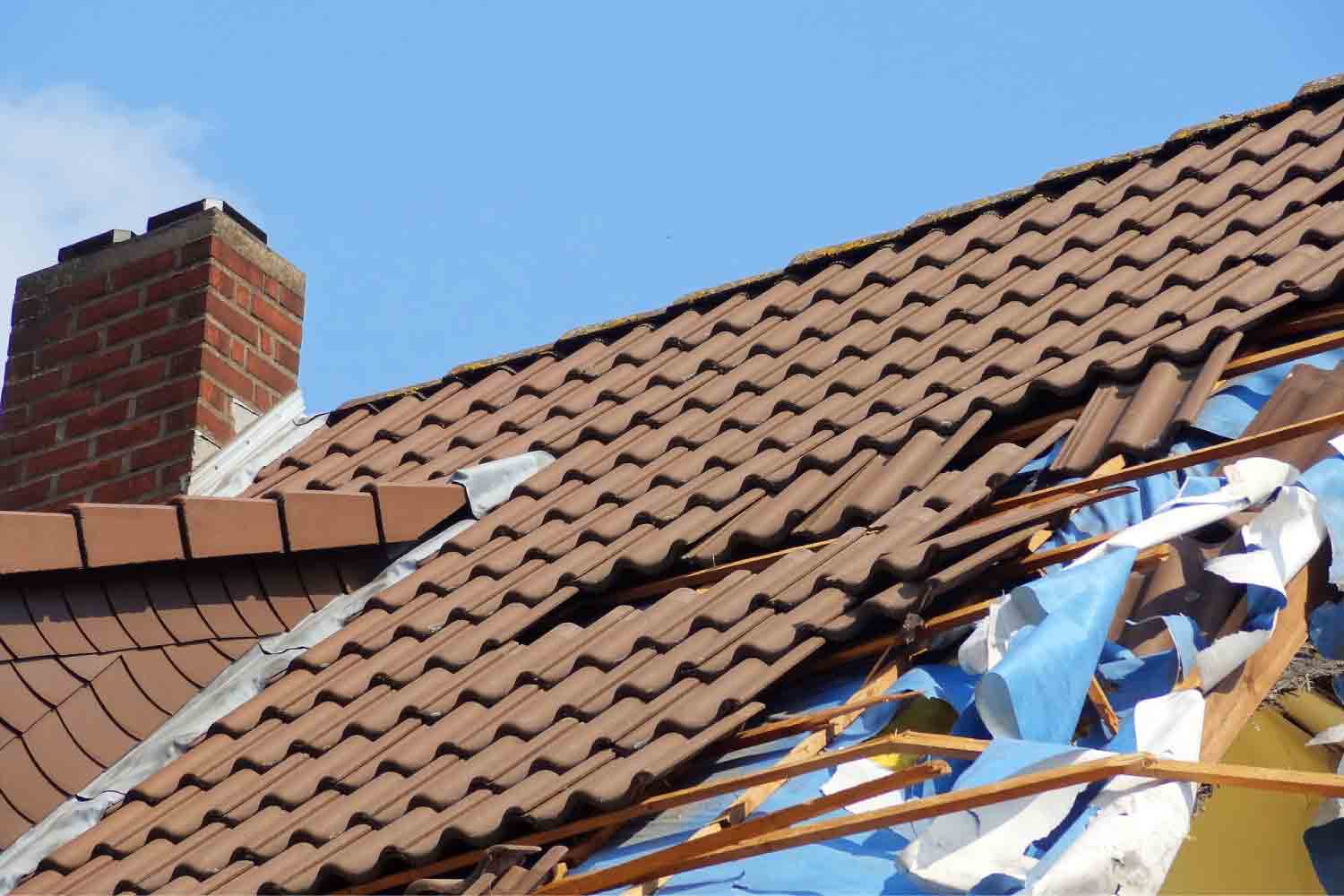 Photo of a tile roof with parts torn off due to a storm.